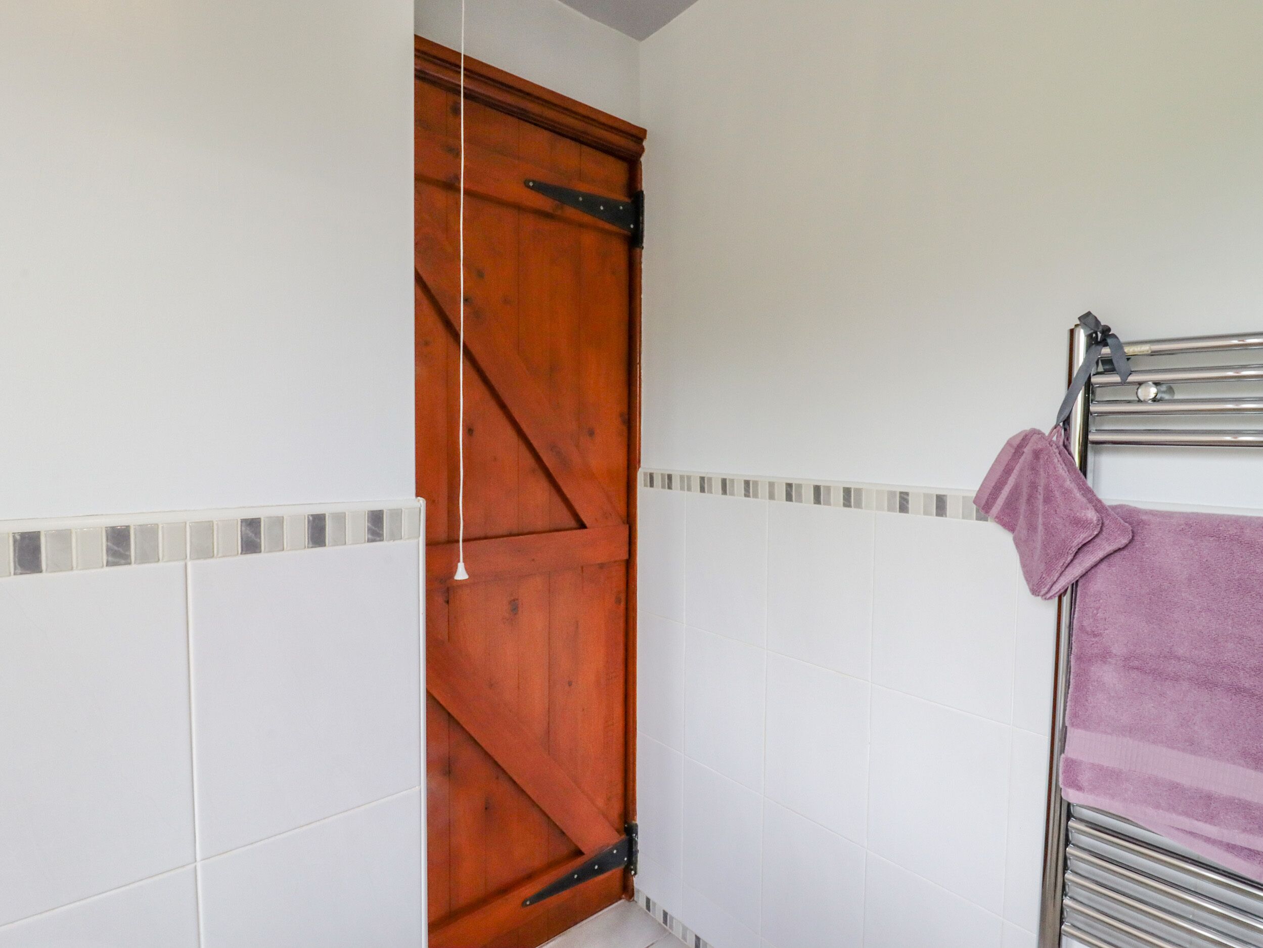 Um banheiro com paredes revestidas de azulejos brancos, uma porta de madeira e um porta-toalhas com uma toalha roxa.