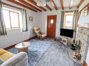 Una sala de estar acogedora con techo de madera, chimenea de piedra, televisor, sofá cómodo y sillón a rayas.