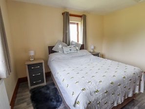Un dormitorio con una cama, dos mesitas de noche, un tocador, una ventana con cortinas y una alfombra oscura.