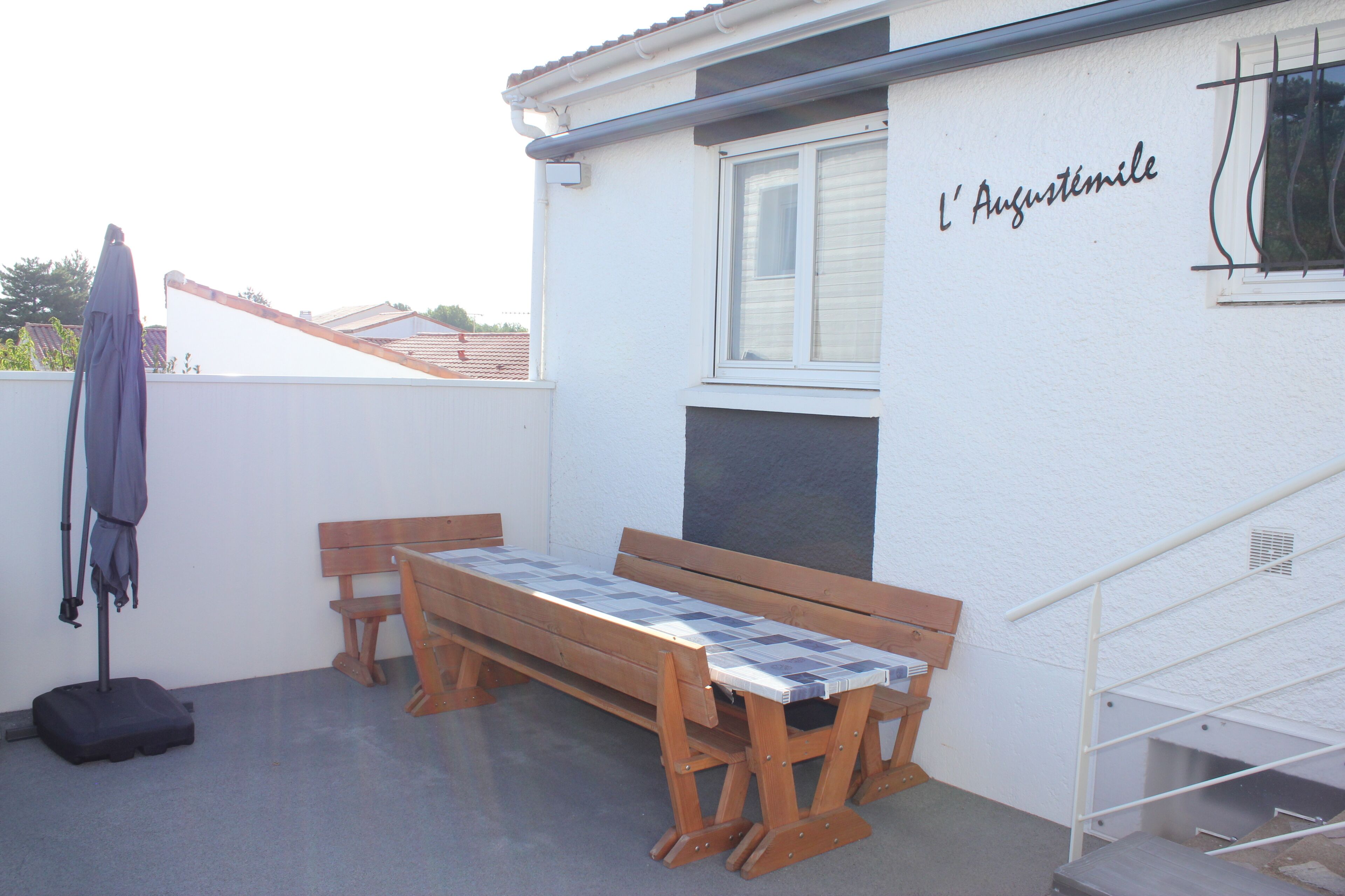 Un balcón con banca de madera, una mesa, un tendedero con una prenda y una ventana con un letrero.