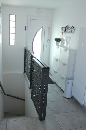 A staircase with a decorative railing, a white door, and a wall with a small potted plant and a shelf with decorative items. - L'augustémile au Bord de L'eau (La Tranche-sur-Mer)