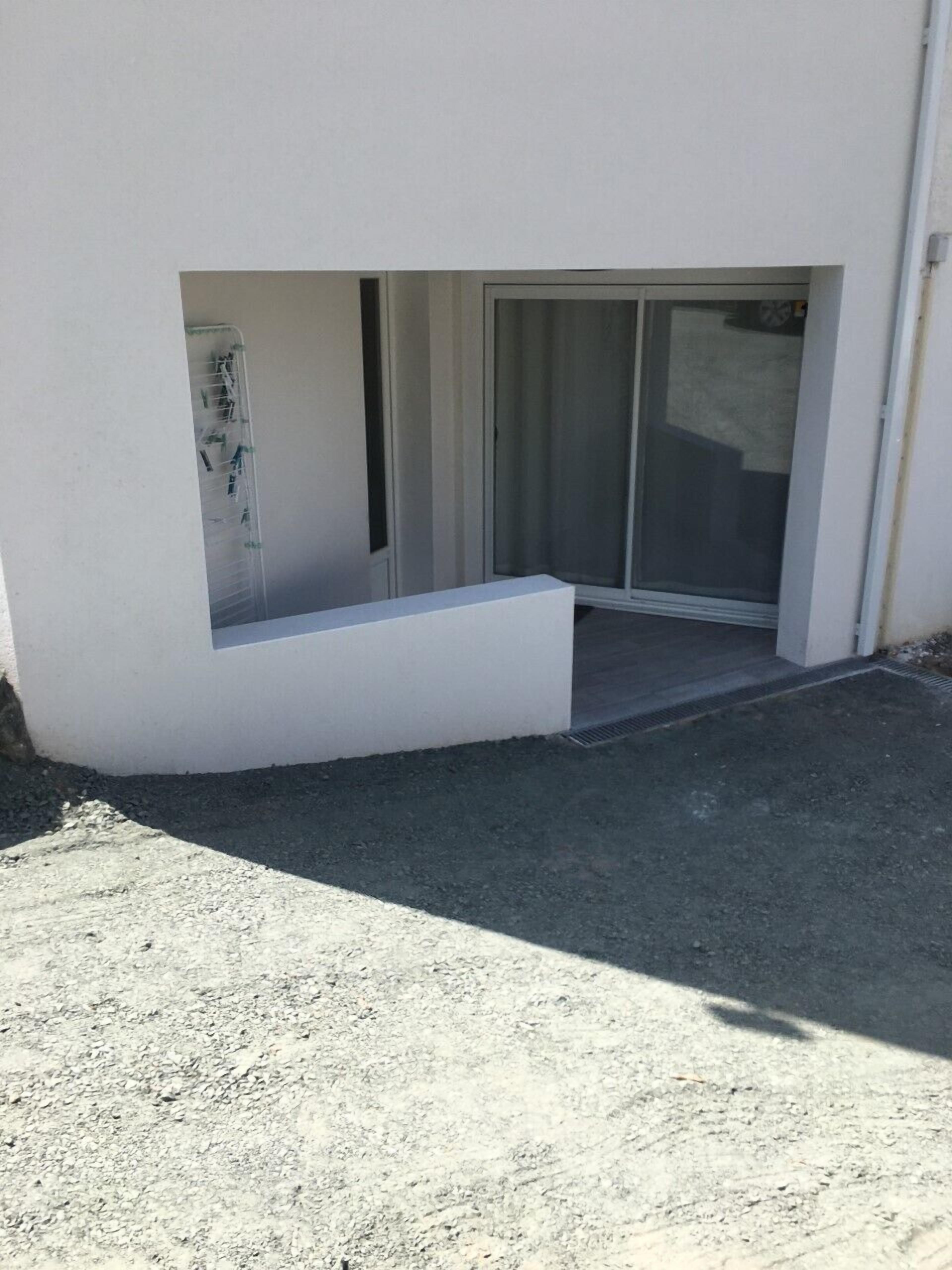 Un bâtiment moderne doté d’un toit plat, d’un petit espace extérieur aménagé pour s’asseoir et d’une porte-fenêtre coulissante donnant sur une entrée abritée.