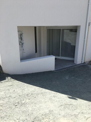 Ein modernes Gebäude mit flachem Dach, einer kleinen Außen-Sitzgelegenheit und einer Schiebetür zu einem überdachten Eingang.