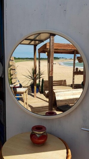 Vista mar d'aquesta platja per una finestra rodona, mobles de fusta i una taula petita amb un objecte vermell a sobre.