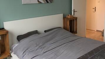 Une chambre à coucher comprenant un lit, une table de chevet, un tableau abstrait accroché au mur, une porte et un luminaire suspendu.