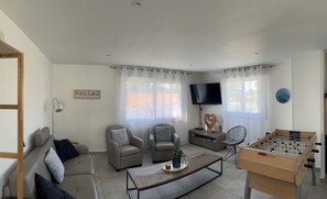 Un saló amb un sofà, butaques, una taula de centre, una televisió i una taula de futbolí.