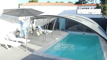 A swimming pool with lounge chairs and umbrellas, surrounded by a covered patio area.