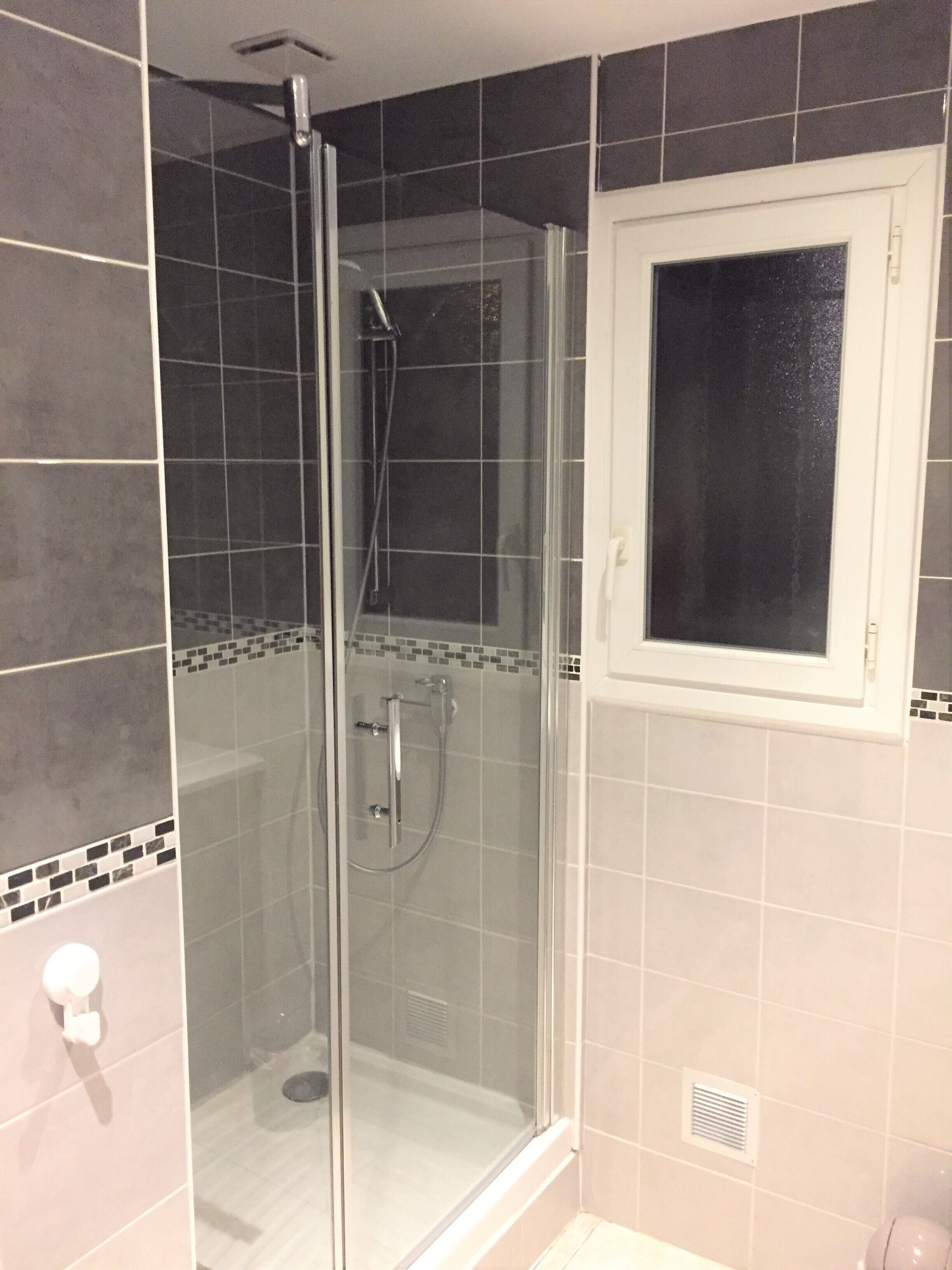 A glass-enclosed shower with a handheld showerhead and a wall-mounted control.
