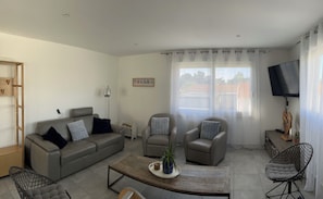 A modern living room with a sofa, two armchairs, a coffee table, and a TV.