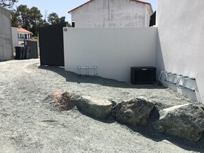 Eine Baustelle mit einem weißen Gebäude, einem schwarzen Tor und einem Kiesplatz mit großen Steinen.