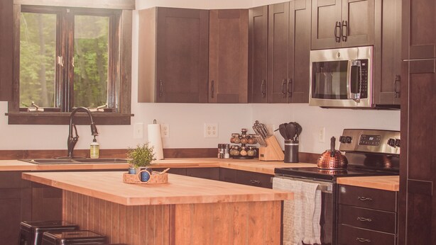 Una cocina con gabinetes de madera, un microondas de acero inoxidable y una isla grande con taburetes.