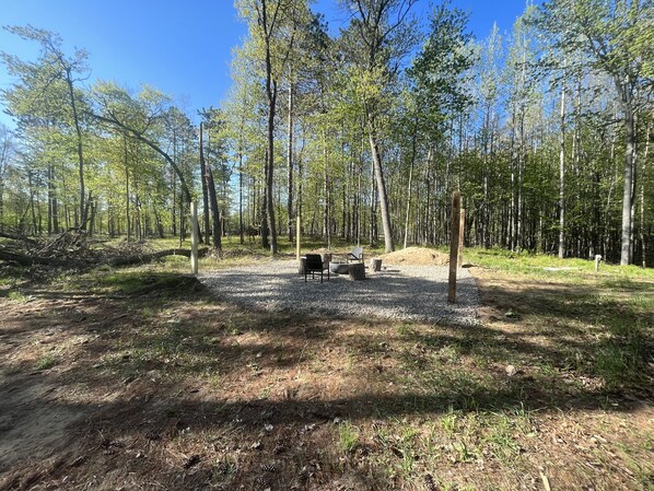 A campground with a fire pit, picnic table, and benches.