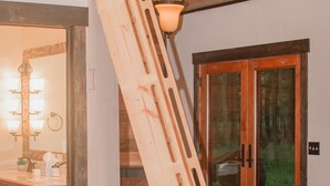 Una mesa de comedor de madera con sillas, una escalera de madera apoyada en la pared y un armario de madera con espejo e iluminación.
