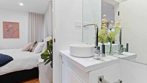 Un baño moderno con un lavabo blanco, espejo y un florero con flores.