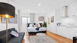 Un dormitorio moderno con una cama grande, un sofá, una mesita redonda y una cocina con armarios blancos y una estufa.