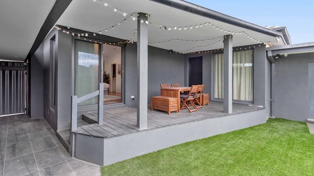Un patio moderno con una mesa y sillas de madera, luces colgantes y una zona cubierta con vistas al interior.