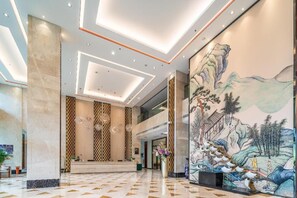 A hotel lobby with a reception desk, patterned columns, and a large mural of a mountainous landscape. - River & Holiday Rezen Hotel Daozhen (Zunyi)