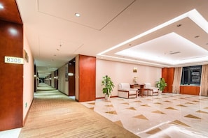 A hotel lobby with a carpeted floor, a reception desk, and a seating area with two chairs and a table.