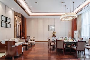 A spacious dining area with a round table set for a meal, flanked by chairs, and a sofa set in the adjacent living area.