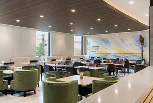 Un restaurante con sillas tapizadas de verde, mesas de madera y un mural de un pájaro en una rama.