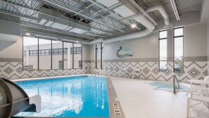 An indoor swimming pool with clear water, surrounded by a tiled floor with depth markers.