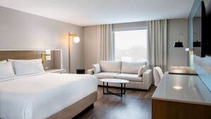 A modern hotel room with a large bed, a sofa, a small table, and a desk.