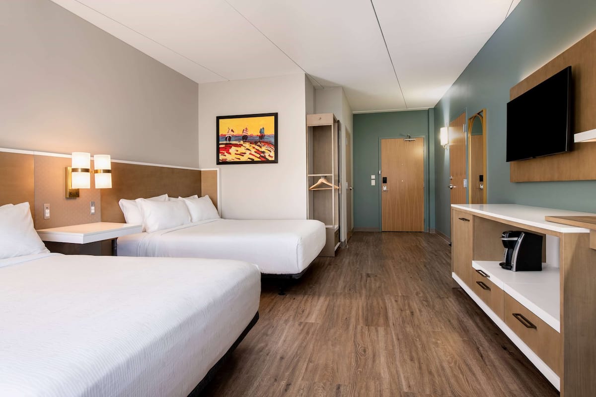 Una habitación de hotel con dos camas, televisión, un cuadro y un armario.