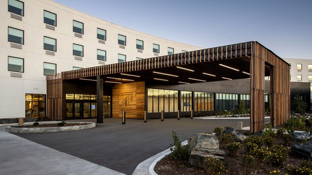 A modern building with a covered entrance, large windows, and a landscaped area with rocks and plants.
