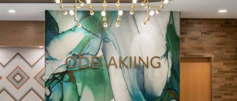 Un mostrador de recepción de diseño moderno, con un cuadro abstracto grande y el nombre 'ODE'AKING' bien visible.