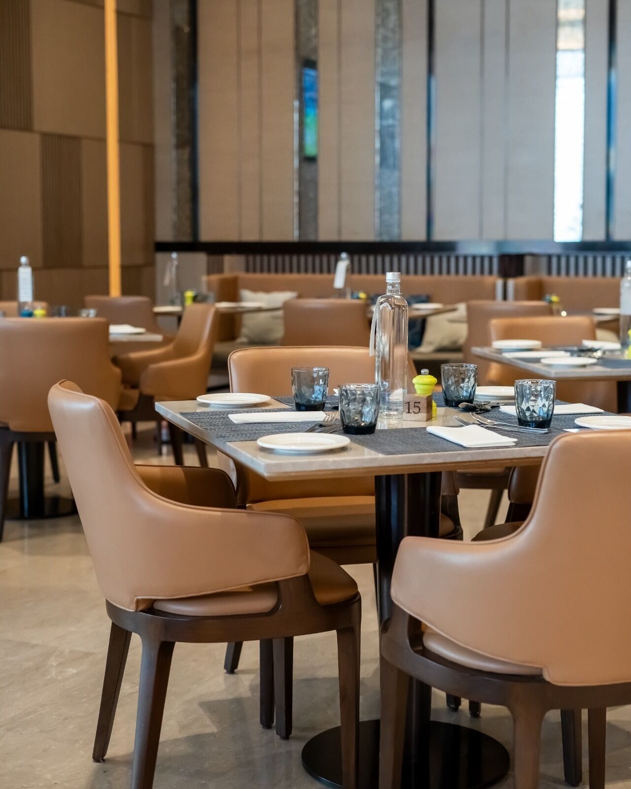Un restaurante con mesas dispuestas para comer, sillas y una botella en la mesa.