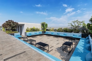 Eine Dachterrasse mit blauen, gepolsterten Sitzgelegenheiten, schwarzen Tischen und einem gefliesten Boden.