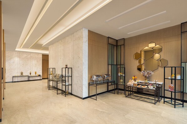 Un moderno vestíbulo de hotel con suelos de mármol, estaciones de buffet y una decoración contemporánea.