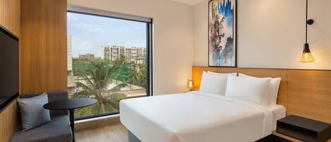 Una habitación de hotel moderna con una cama grande, un área de descanso, un ventanal con vistas a la ciudad y un cuadro en la pared.