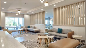 Un hall d’hôtel moderne, doté d’espaces aménagés avec des sièges, d’un comptoir d’accueil et de grandes fenêtres laissant entrer la lumière naturelle.