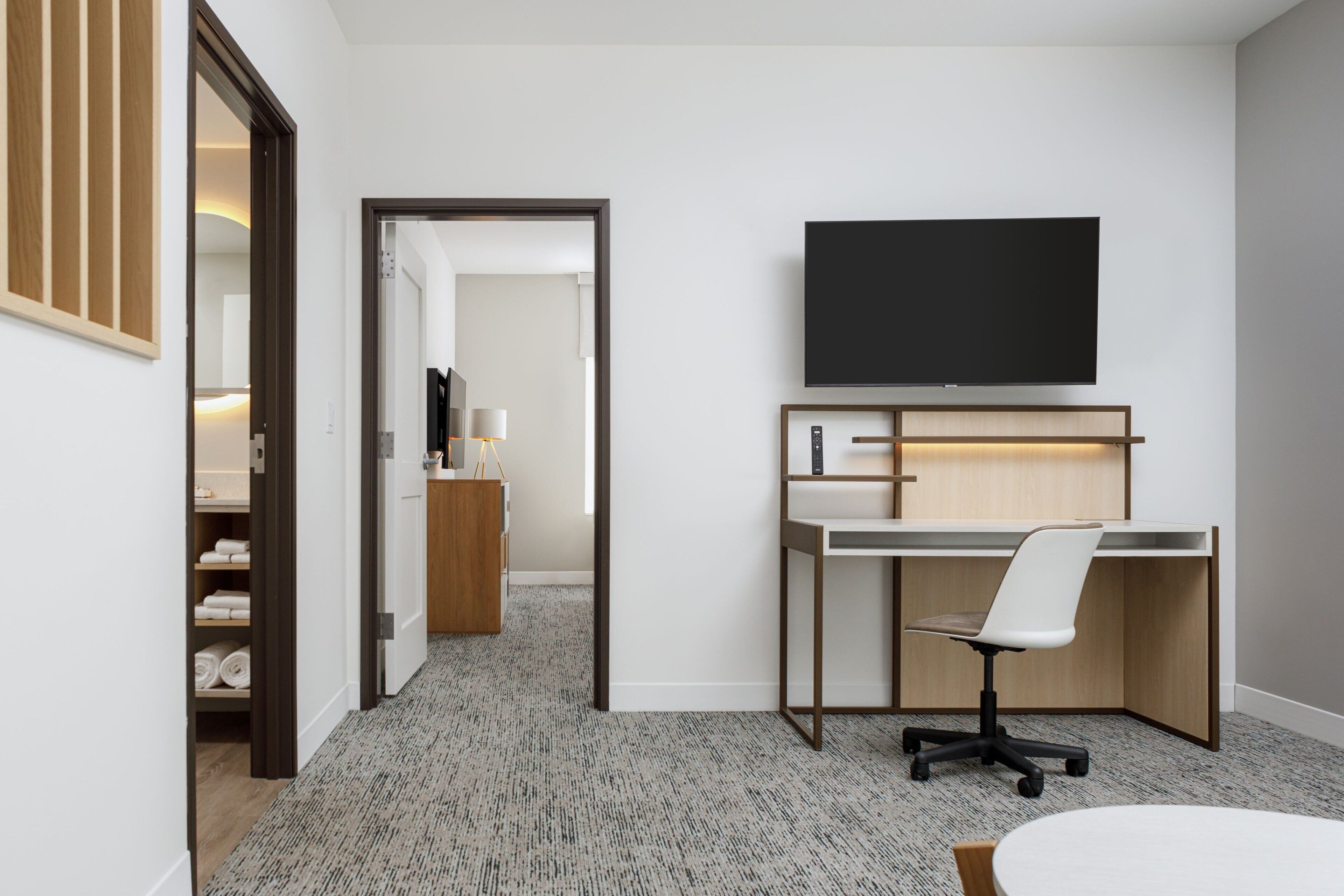 A modern hotel room with a desk, chair, and a flat-screen TV mounted on the wall.