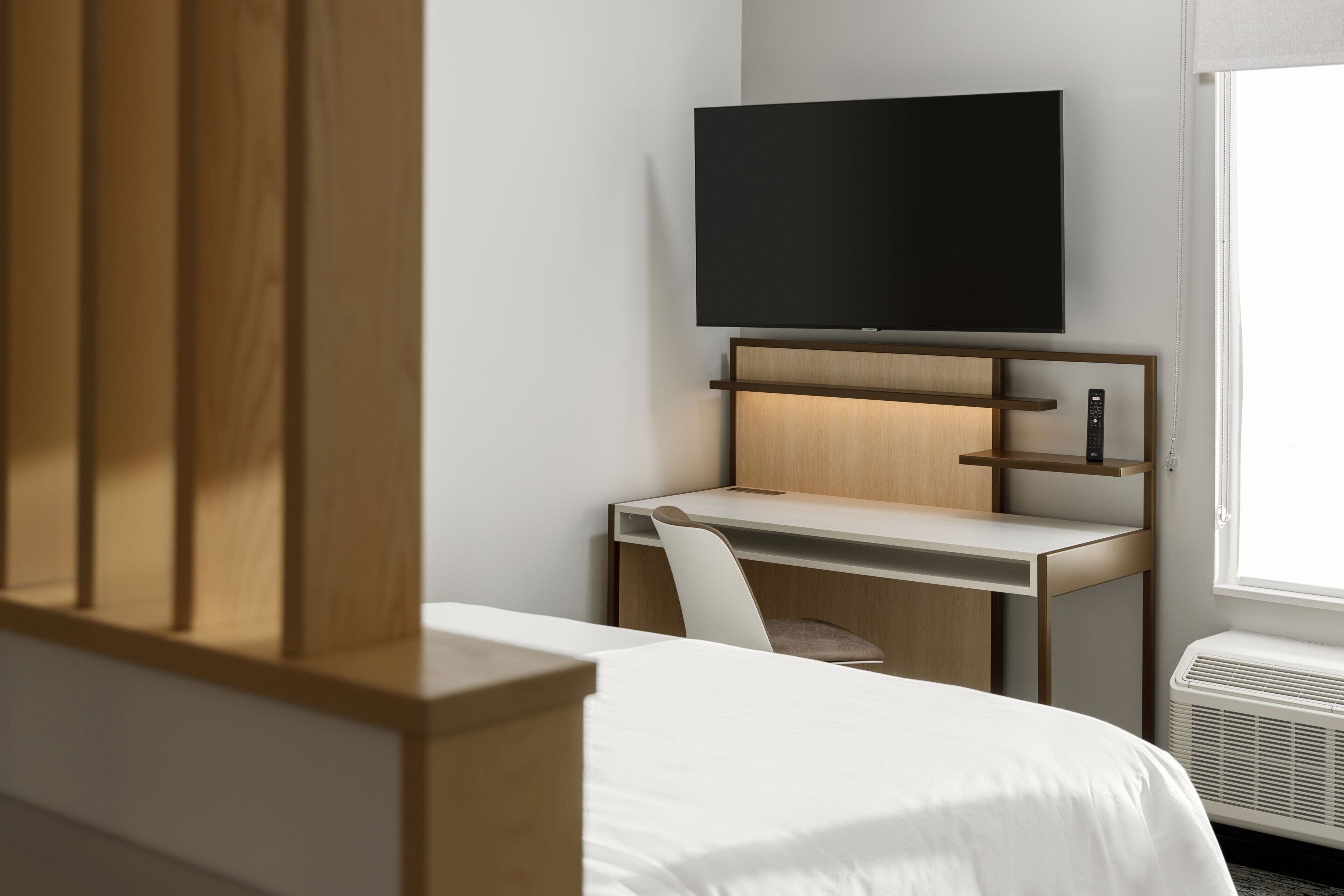Une chambre d’hôtel comprenant un lit, un bureau avec une chaise, un téléviseur fixé au-dessus du bureau et une fenêtre donnant sur un paysage agréable.