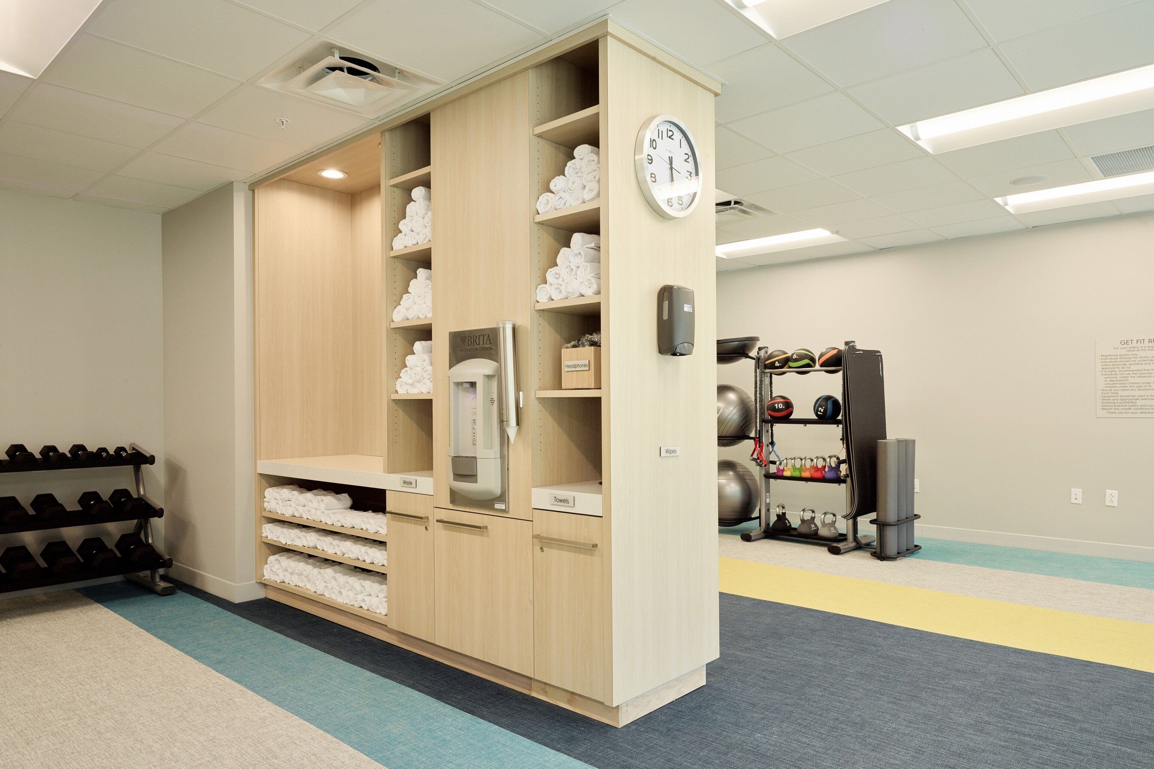 A locker room with wooden lockers, a clock, and a rack of dumbbells.