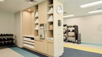 A locker room with wooden lockers, a clock, and a rack of dumbbells.