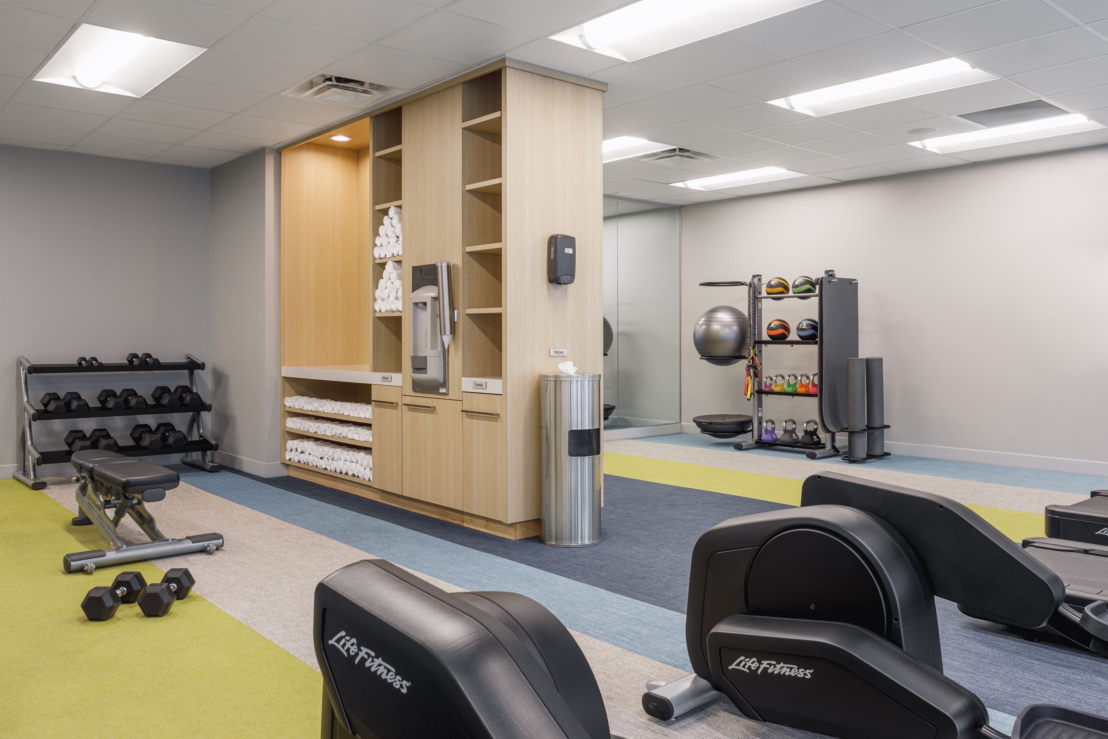 Un gimnasio con equipamiento de levantamiento de pesas, mancuernas y máquinas de ejercicio.