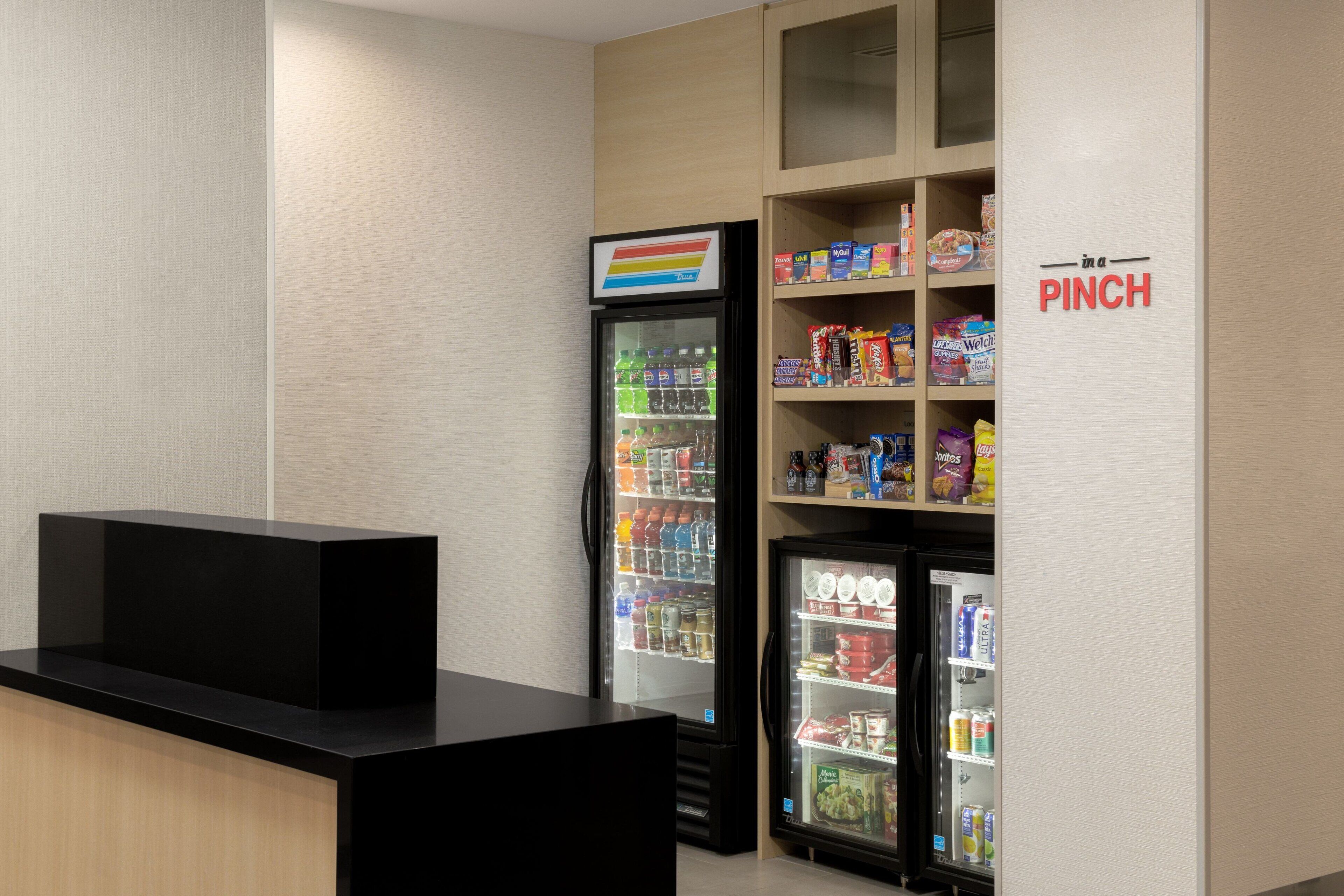 A vending area with a refrigerator stocked with beverages and snacks, a counter, and a sign indicating a 'PINCH' section.
