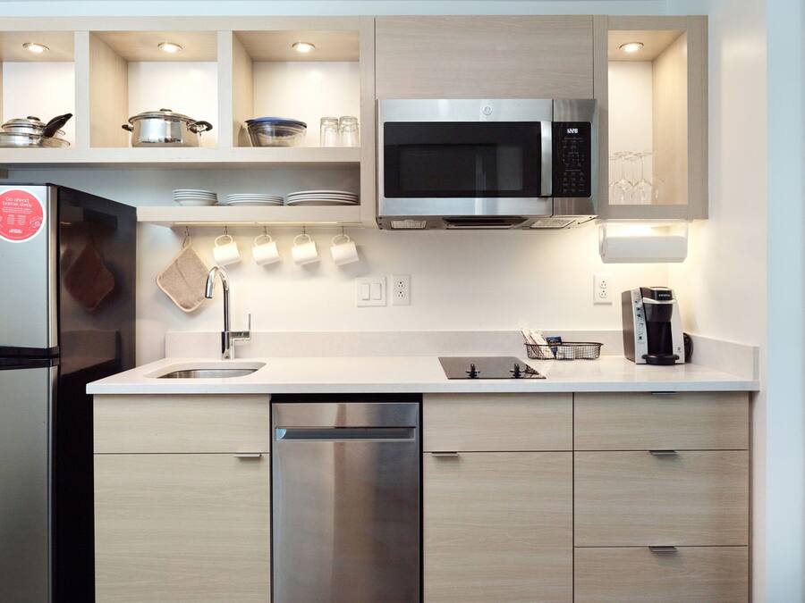 A modern kitchen with a stainless steel refrigerator, microwave, and dishwasher. There are wooden cabinets and a white countertop.