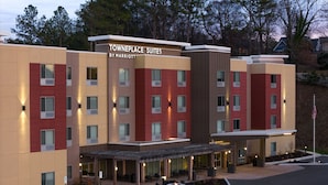 Un hôtel à plusieurs étages au design moderne, avec une façade composée d’un mélange de panneaux beiges et rouges, une entrée couverte dotée d’un espace salon extérieur et un mât sur lequel flotte le drapeau américain.