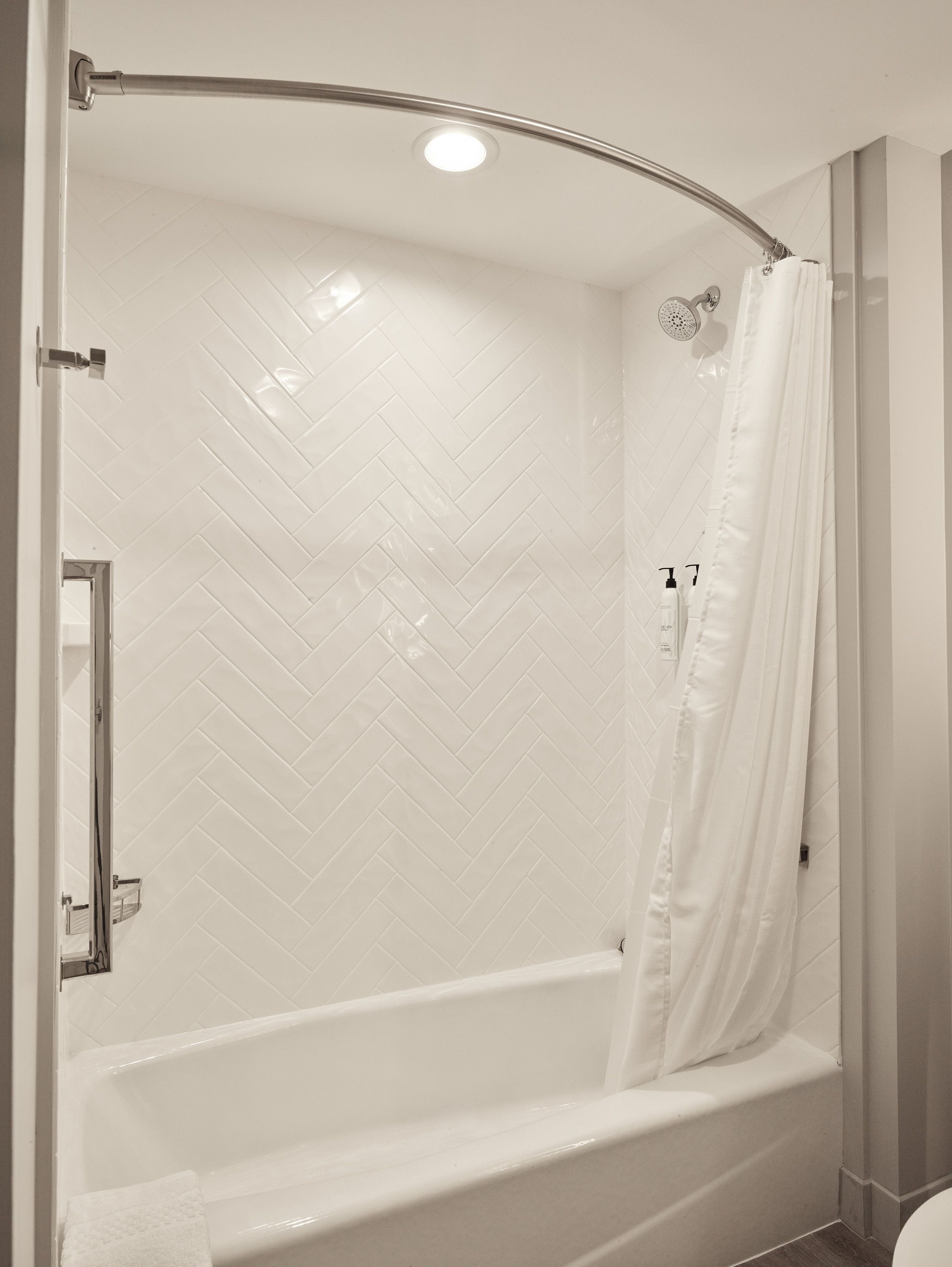 A modern bathroom with a curved shower enclosure, white herringbone tile, a glass shower door, and a visible toilet.