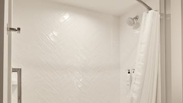 A modern bathroom with a curved shower enclosure, white herringbone tile, a glass shower door, and a visible toilet.