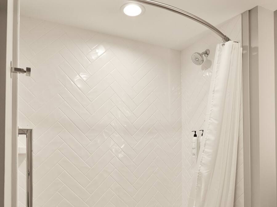 A modern bathroom with a curved shower enclosure, white herringbone tile, a glass shower door, and a visible toilet.