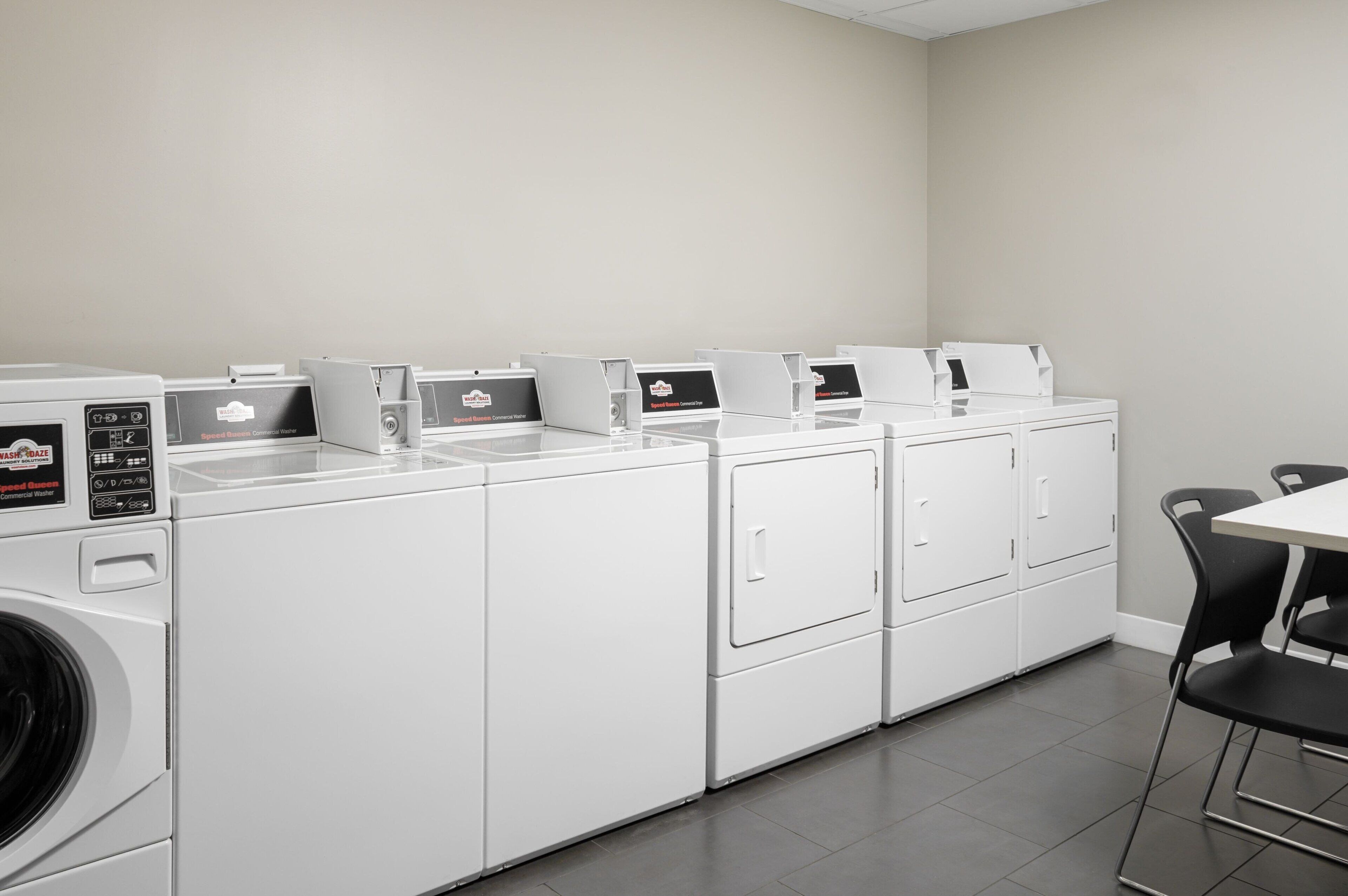 Une buanderie équipée de plusieurs machines à laver et de plusieurs sèche-linge, une table avec des chaises et un mur uni.