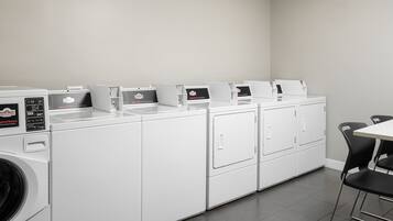 Une buanderie équipée de plusieurs machines à laver et de plusieurs sèche-linge, une table avec des chaises et un mur uni.