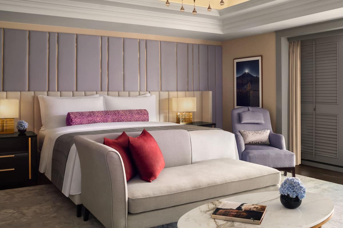 A hotel room with a large bed, a grey sofa, a chair, a nightstand, and a round coffee table.