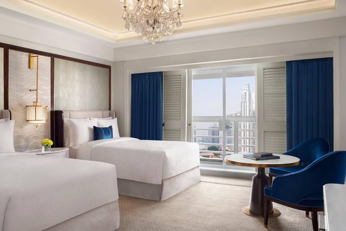 A hotel room with two beds, a chandelier, a round table, and a view of the city.