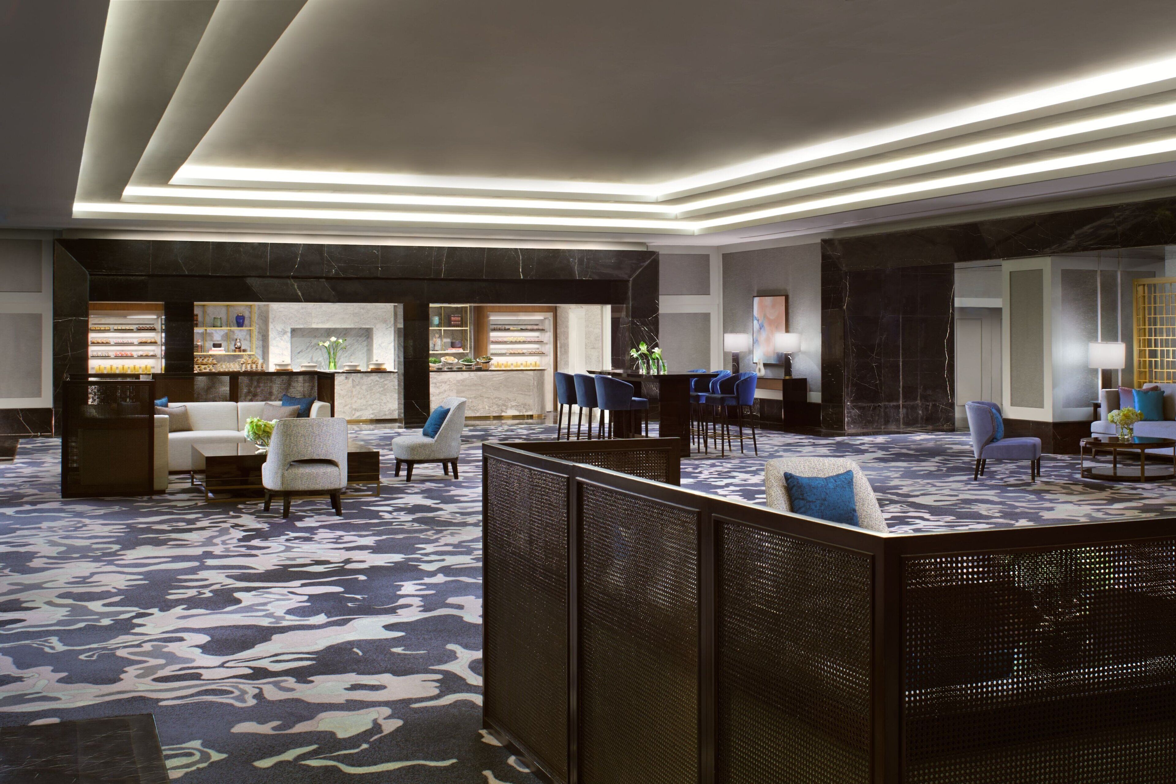 A modern lobby with seating areas, a reception desk, and a patterned carpet.